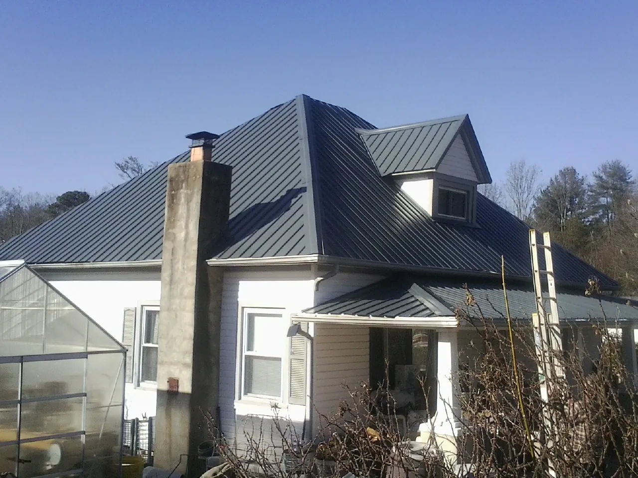 Dark blue standing seam metal roof on a white farmhouse with dormer — Slate & Tile Roof Repair by Roofing Brothers in Cabin John