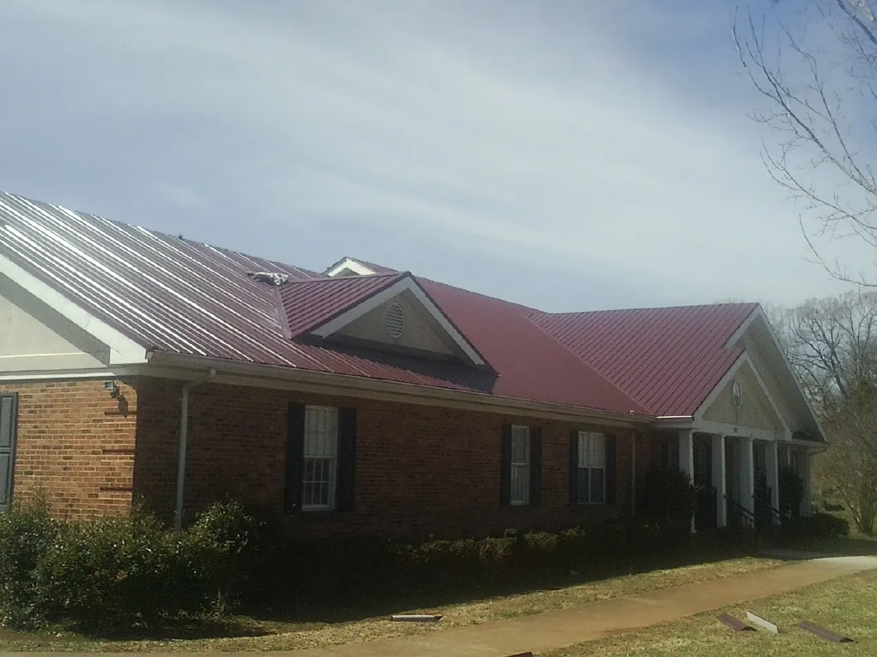 Red metal roof with gabled entries on a long brick building, from a Hail Damage Roof Repair job in Cabin John