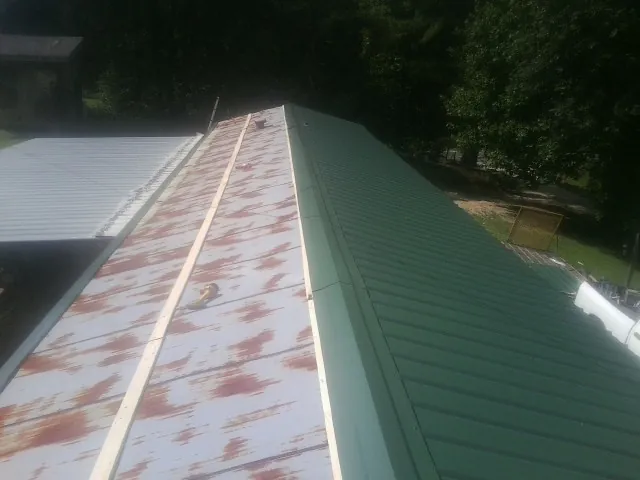 Old rusted panels beside newly installed green metal roofing — Wind Damage Roof Repair by Roofing Brothers in Cabin John