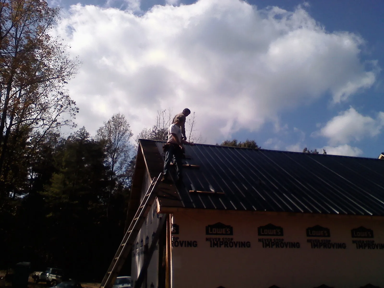 Roofer fastening dark metal panels high against a cloudy sky, from a Roof Inspection job in Cabin John